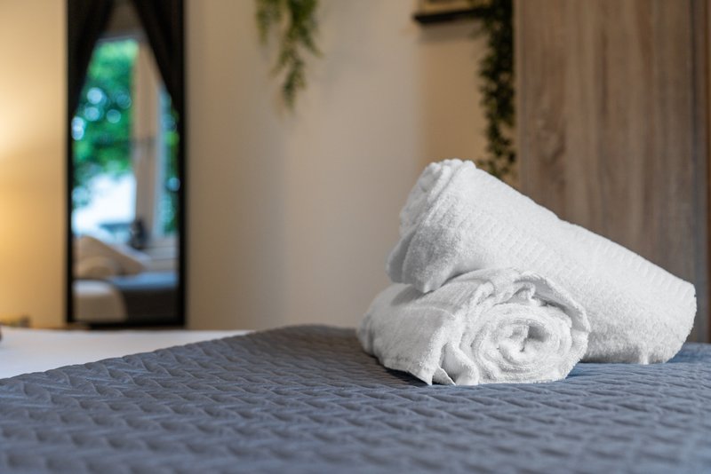 Rolled white towels on bed with lamp and window view in background