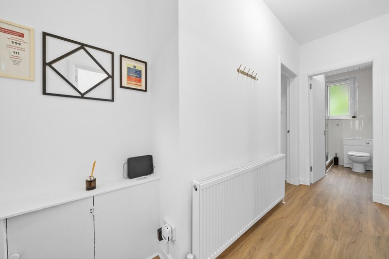 Bright hallway with white walls, wooden floor, radiator and wall art