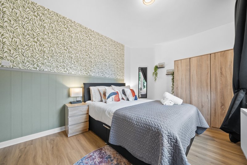 Modern bedroom with double bed, patterned wallpaper, wooden flooring and bedside table