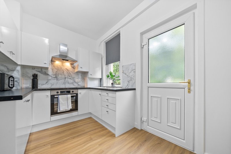 Modern white kitchen with marble backsplash, wooden floor and door to garden