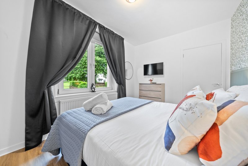 Bright bedroom with double bed, black curtains, window with garden view, wooden floor