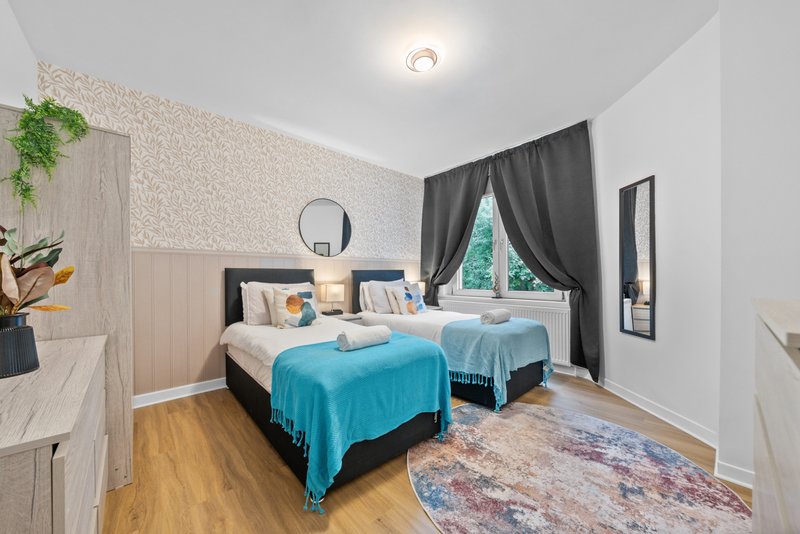 Bedroom with two single beds, blue throw blankets, wooden floor and decorative rug
