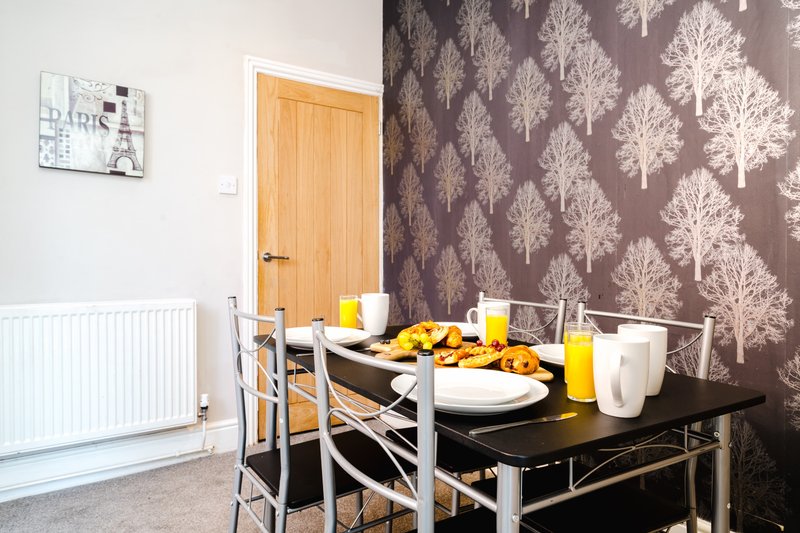 Dining area with black table, chairs, place settings, yellow accessories and patterned wallpaper