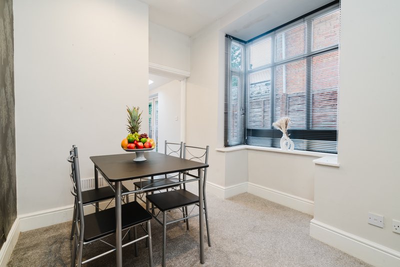 Bright dining area with table, chairs, fruit bowl, and large windows overlooking street
