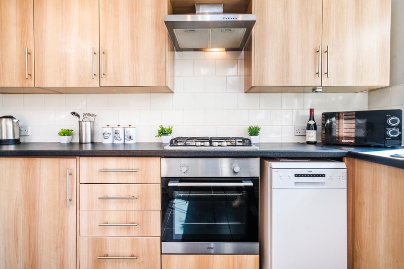Modern kitchen with light wood cabinets, black countertop, stainless steel appliances and white tile backsplash