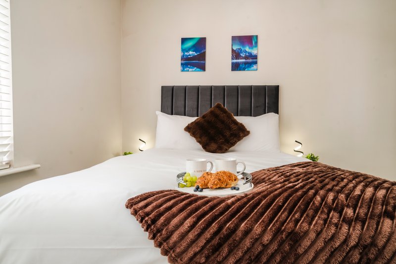 Modern bedroom with double bed, gray headboard, white bedding, brown throw blanket, and welcome breakfast tray