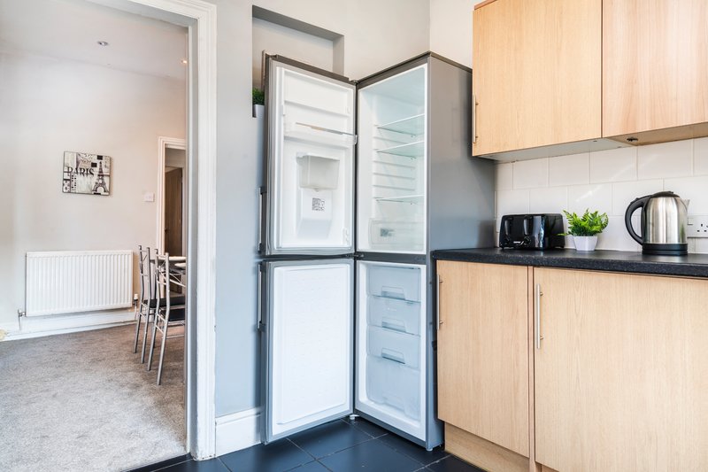 Modern kitchen with light wood cabinets, open refrigerator, black countertop and small appliances