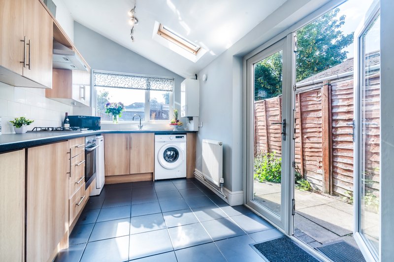 Modern kitchen with light wood cabinets, integrated appliances, and sliding doors to garden