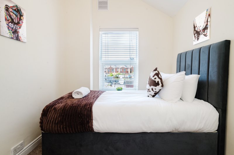 Bedroom with black upholstered bed, white bedding, brown throw, window with city view