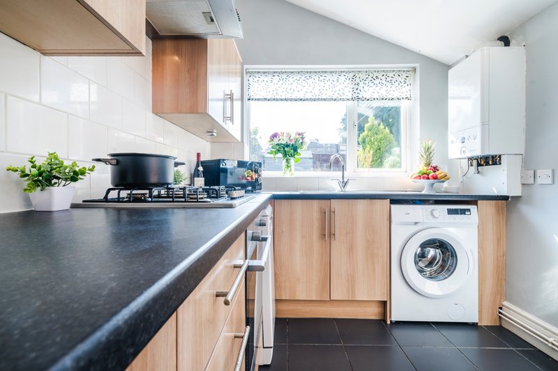 Modern kitchen with dark countertops, wooden cabinets, washing machine and garden view