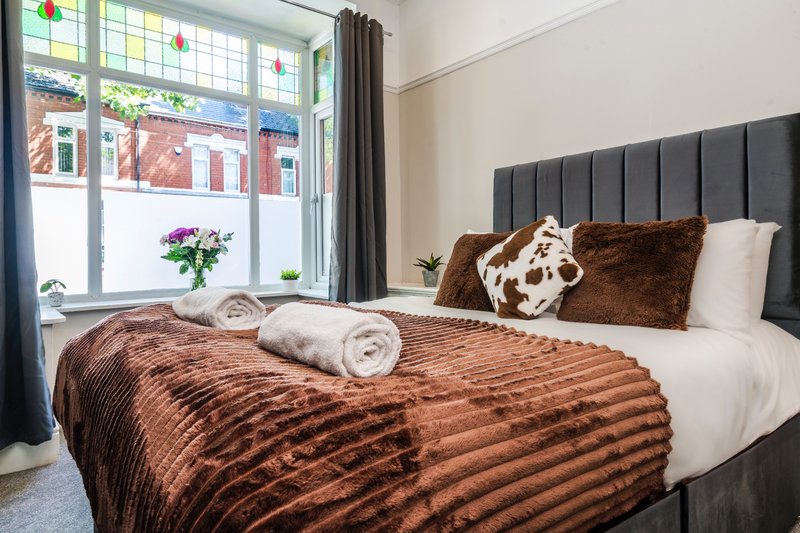 Modern bedroom with brown textured bedding, black headboard, rolled towels, and large window with street view