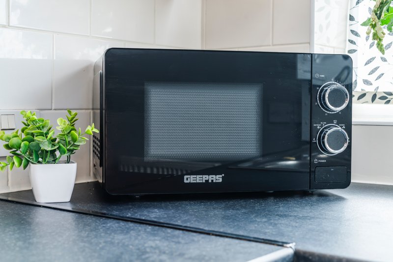Black microwave oven on kitchen counter with potted plant and window behind