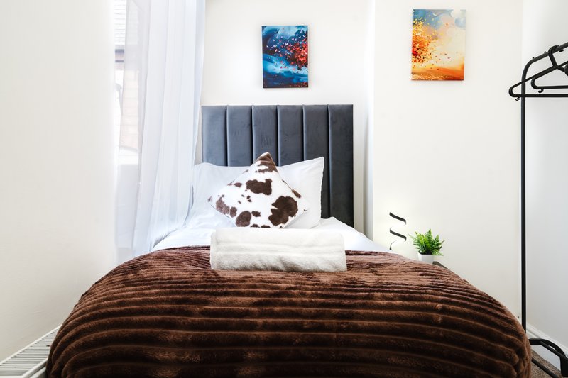 Bedroom with grey headboard, brown textured bedding, white pillows and decorative wall art