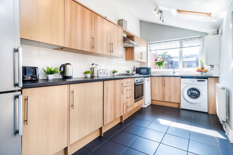 Modern kitchen with light wood cabinets, black countertop, stainless steel appliances and natural light
