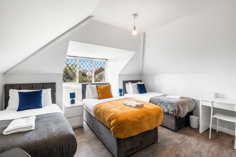 Bright attic bedroom with two beds, orange and blue bedding, white desk and sloped ceiling