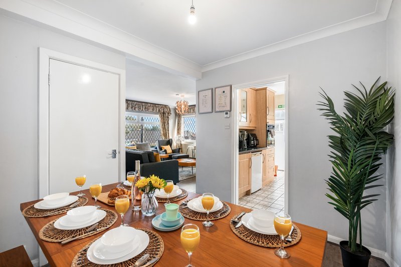 Dining room with wooden table set for four, white plates, yellow flowers and candles, open-plan kitchen visible beyond