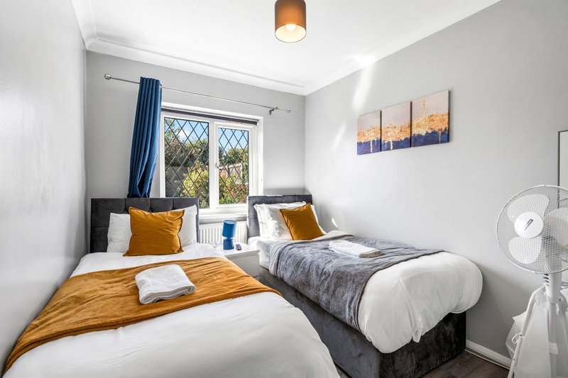 Bright twin bedroom with white walls, two single beds, blue curtains, and window view