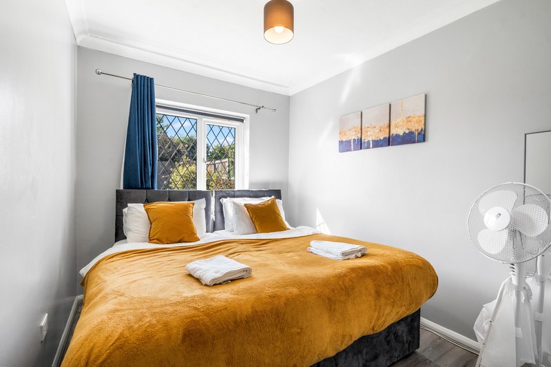 Bright bedroom with double bed, yellow bedding, blue curtains and white fan
