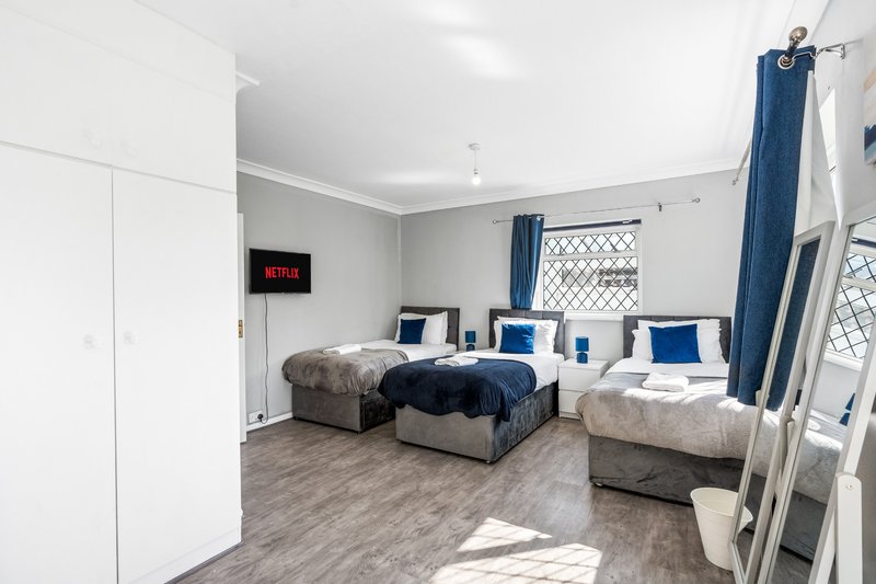 Bright dormitory bedroom with multiple beds, blue bedding, wooden flooring and windows