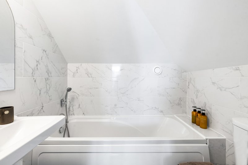 Modern bathroom with marble tile walls, soaking tub, chrome fixtures and skylight
