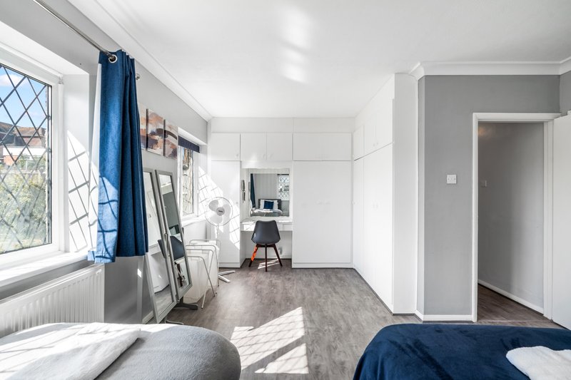 Bright modern bedroom with double bed, desk area, blue curtains and wooden floor