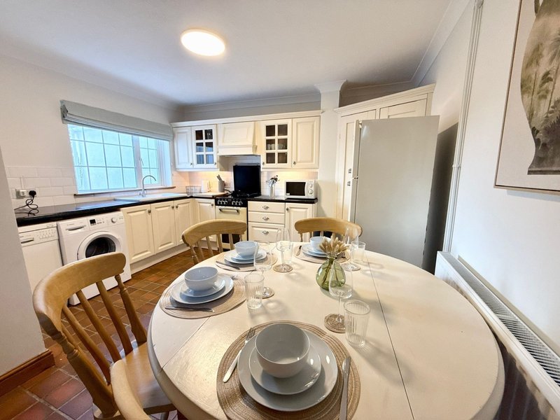Open-plan kitchen-diner with cream cabinetry, round dining table set for a meal, and wooden chairs
