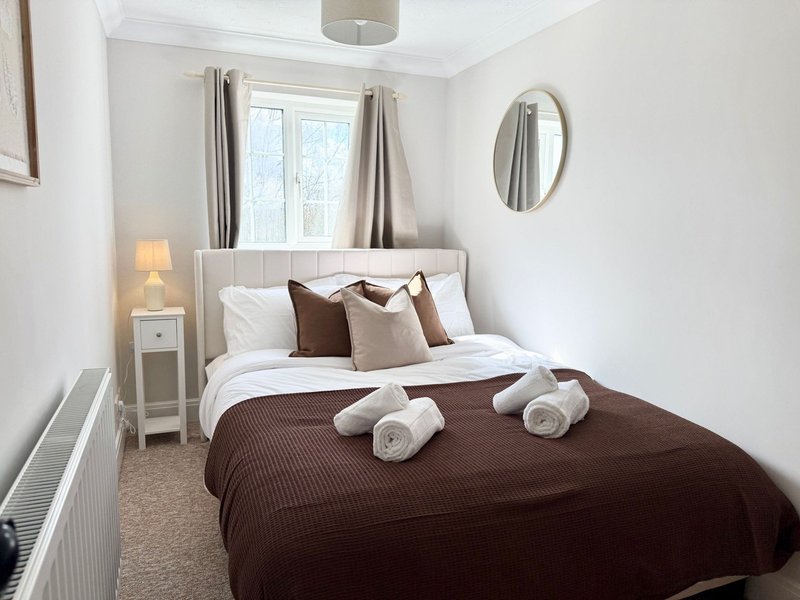 Bright bedroom with double bed, brown bedding, white pillows, rolled towels, and oval mirror