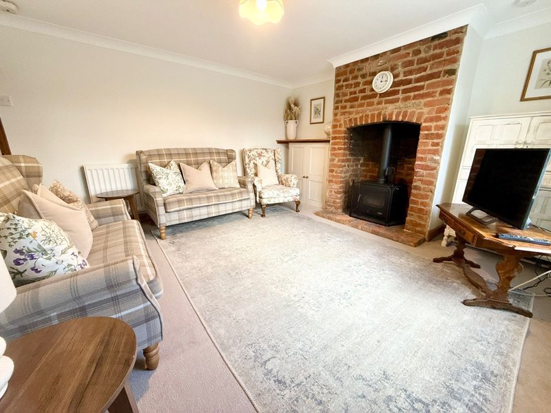 Spacious living room with brick fireplace, upholstered armchairs, sofa, wooden coffee table and television