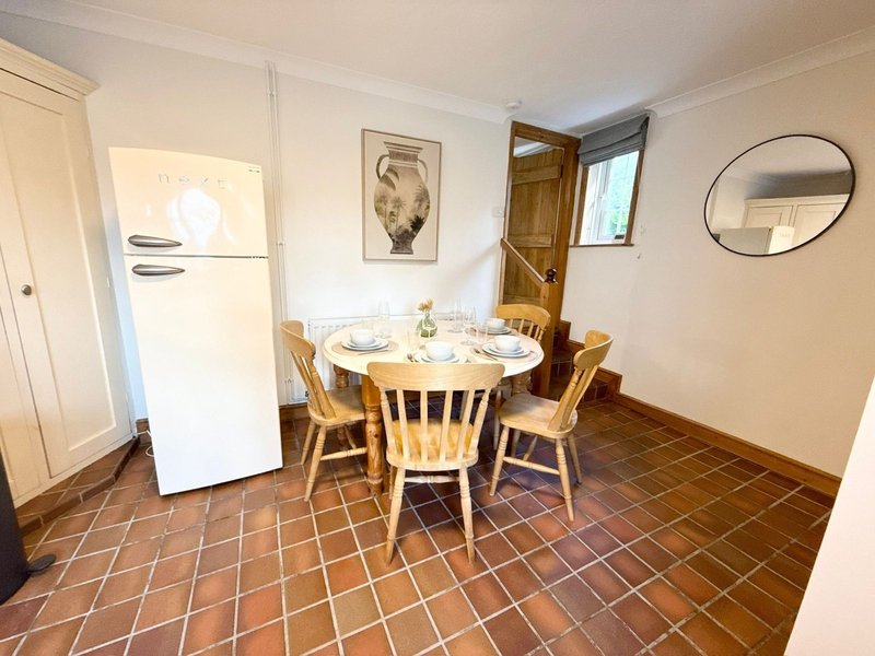 Kitchen-dining area with round wooden table, chairs, cream refrigerator and terracotta tile floor