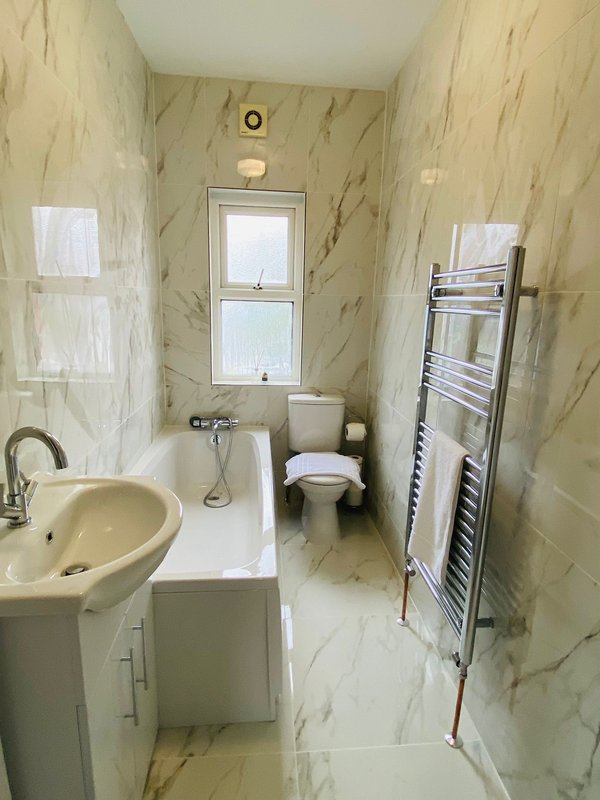 Modern bathroom with marble-effect tiles, sink, toilet, heated towel rail and window