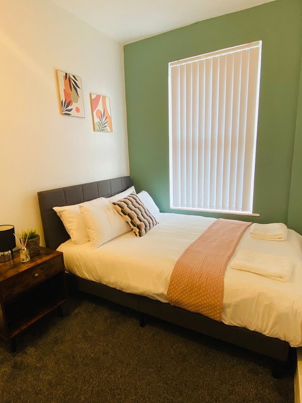 Bedroom with double bed, yellow bedding, green accent wall and vertical blinds