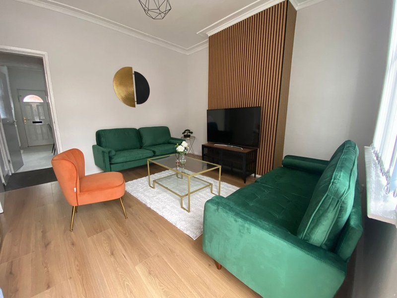 Modern living room with green velvet sofas, orange accent chair, wooden flooring and TV
