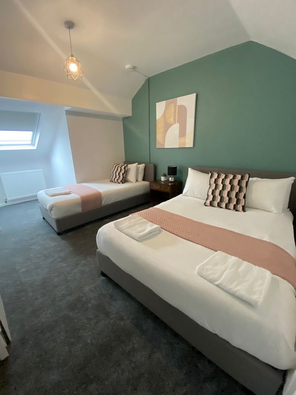 Modern twin bedroom with two beds, green accent wall, pendant light and framed artwork