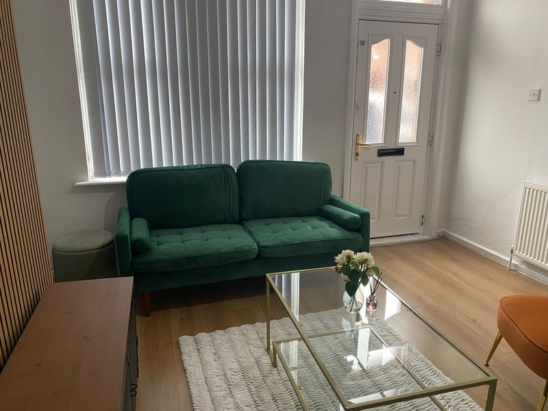 Living room with green velvet sofa, glass coffee table, white flowers in vase, wooden floor