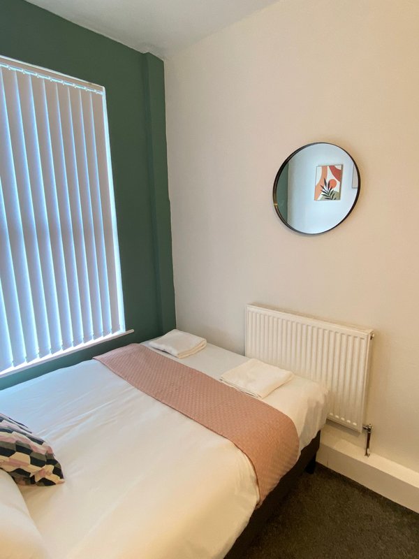 Bedroom with single bed, green accent wall, radiator and round mirror