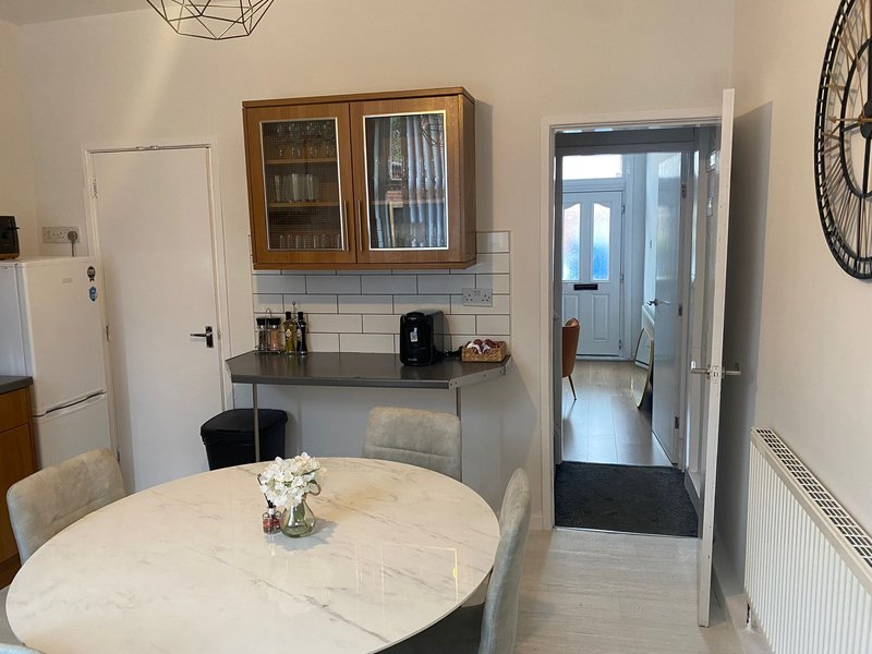 Modern kitchen and dining area with round white table, wall-mounted shelving, and open doorway to hallway