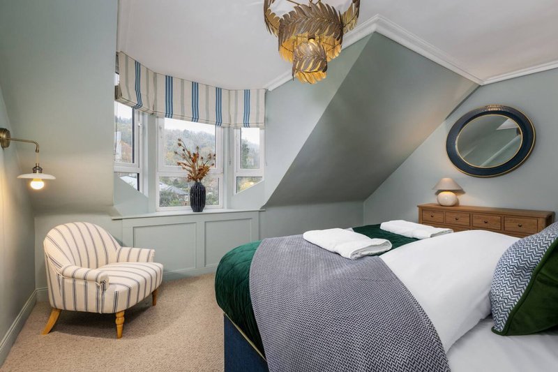 Modern bedroom with double bed, striped armchair, sloped ceiling and window with blinds