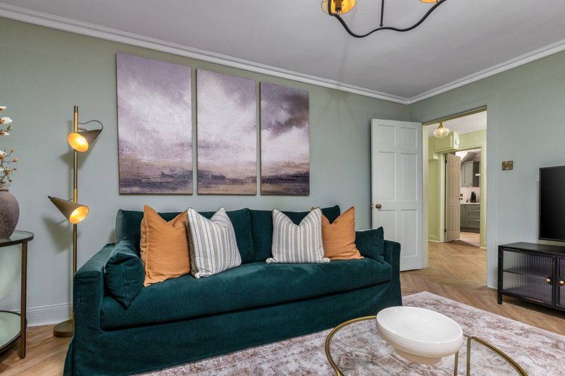 Living room with teal velvet sofa, orange and striped cushions, wall art, and modern furnishings