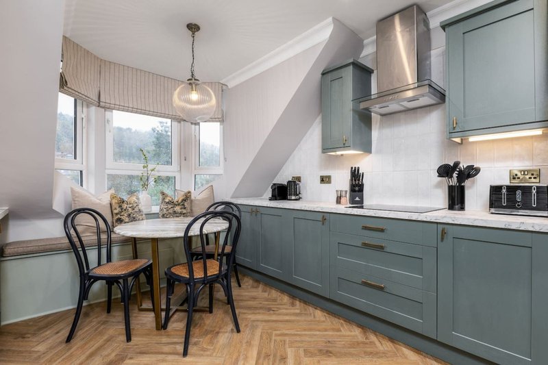 Modern kitchen with blue cabinetry, dining table, pendant light, and window overlooking garden