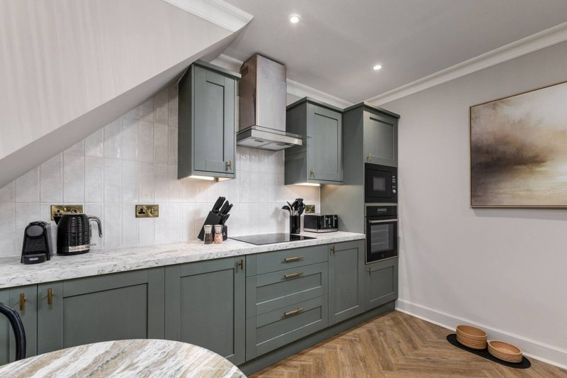 Modern kitchen with sage green cabinetry, white marble countertops, stainless steel appliances and herringbone flooring