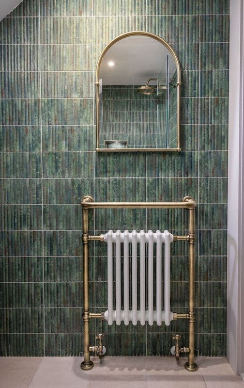 Bathroom with green tile wall, arched mirror, and brass towel rail radiator