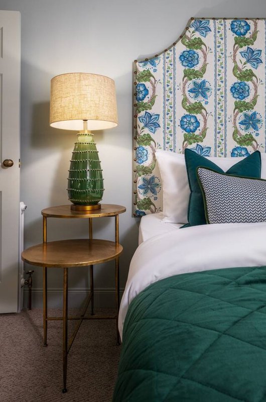 Bedroom with double bed, green bedding, wooden side table, table lamp, and floral headboard