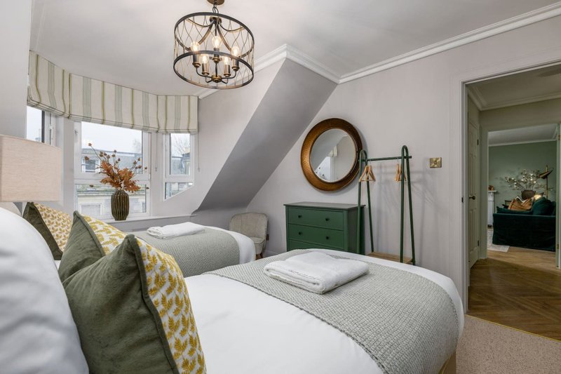 Bright attic bedroom with two single beds, patterned cushions, round mirror and wooden flooring