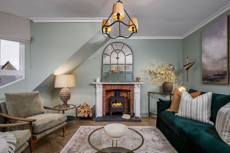 Living room with fireplace, beige armchair, green sofa, decorative mirror and pendant light