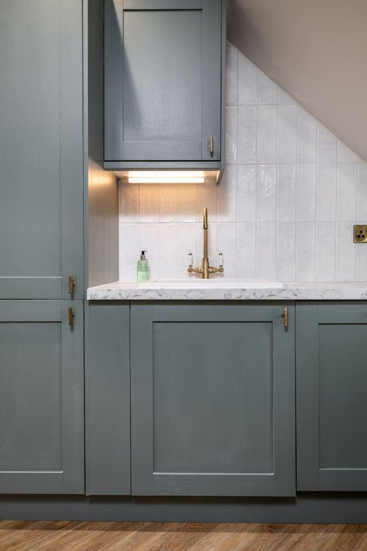 Modern kitchen with gray cabinetry, white subway tile backsplash, marble countertop and brass faucet