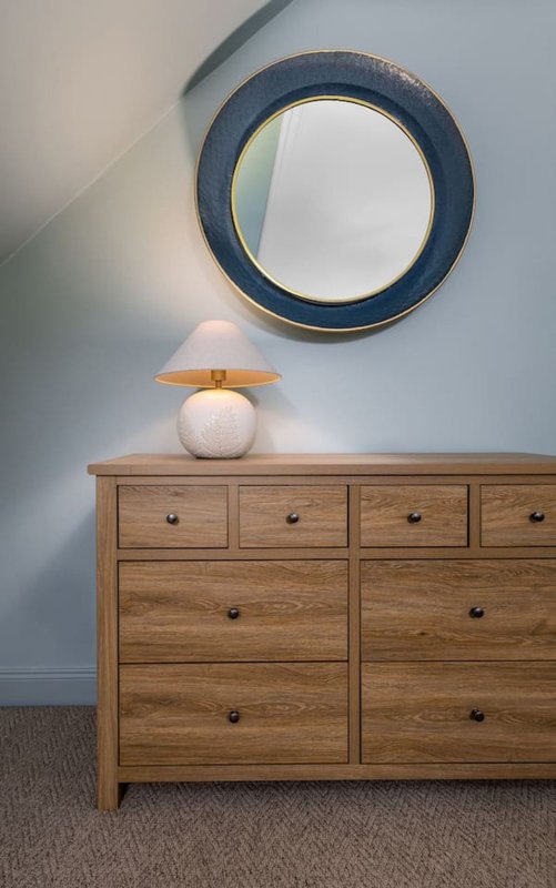 Wooden dresser with round table lamp beneath circular wall mirror