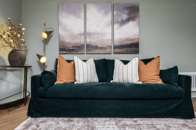 Living room with dark blue sofa, decorative pillows, wall art, and side table with vase