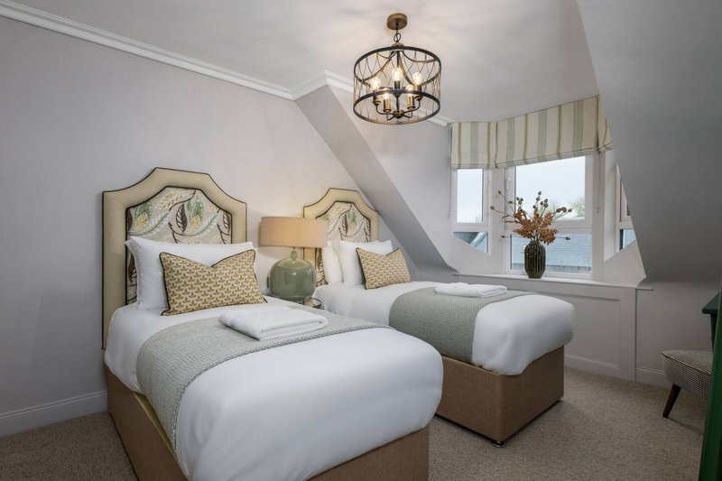 Bright twin bedroom with upholstered headboards, white bedding, pendant light and bay window