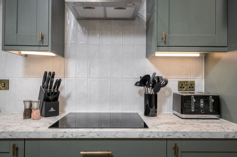Modern kitchen with sage-green cabinetry, marble countertop, induction hob, and kitchen utensil storage