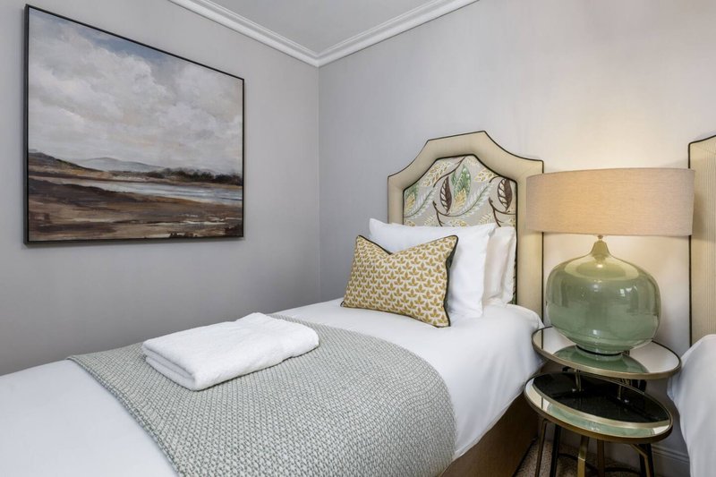 Modern bedroom with single bed, framed landscape artwork, green table lamp and neutral decor